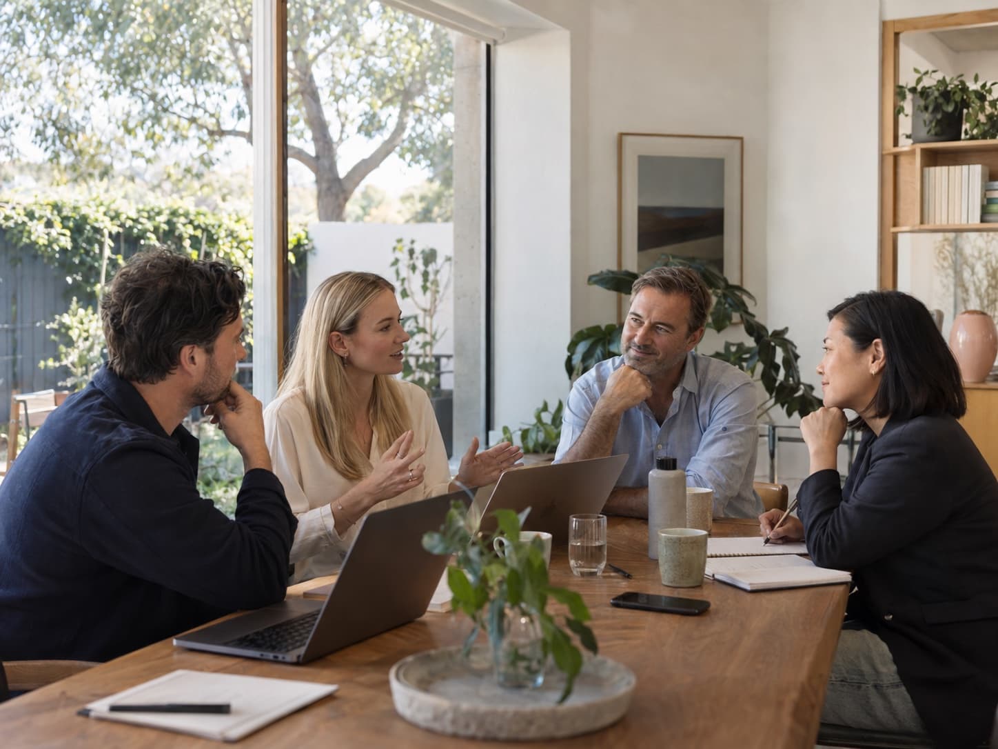Illustrative scene of four colleagues sharing ideas in a bright Australian office overlooking a leafy courtyard.